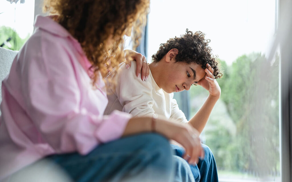 Upset boy sitting on sofa while his mother looking at him.