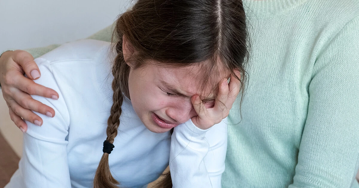 Distressed child crying while being comforted by her parent.