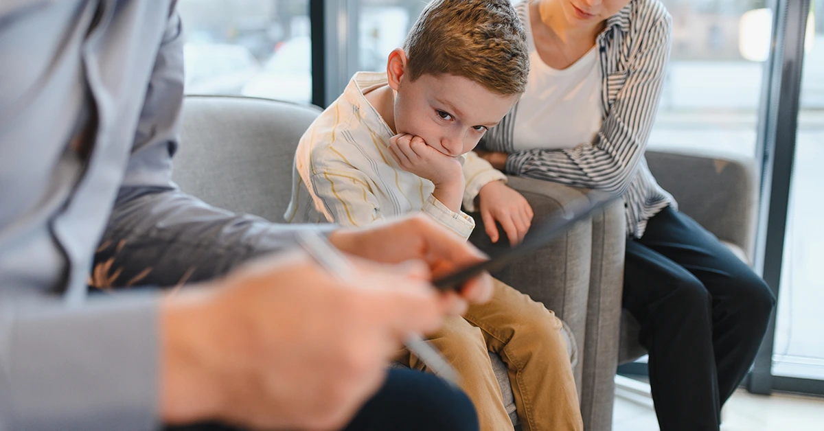 Young boy appearing withdrawn during a counseling session with a parent and mental health professional.