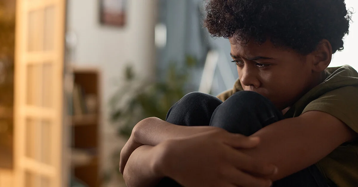 Distressed boy sitting alone with knees pulled to his chest, showing signs of emotional overwhelm.